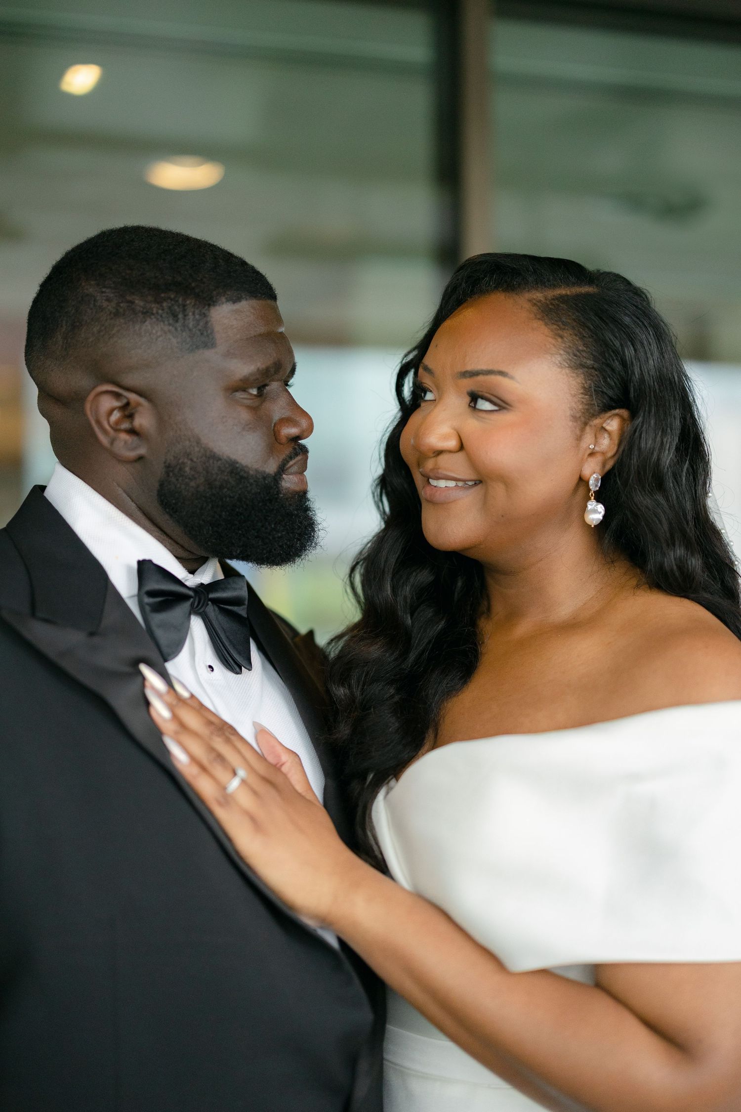 A bride and groom share an intimate moment, dressed in elegant wedding attire, with the bride in an off-shoulder gown.