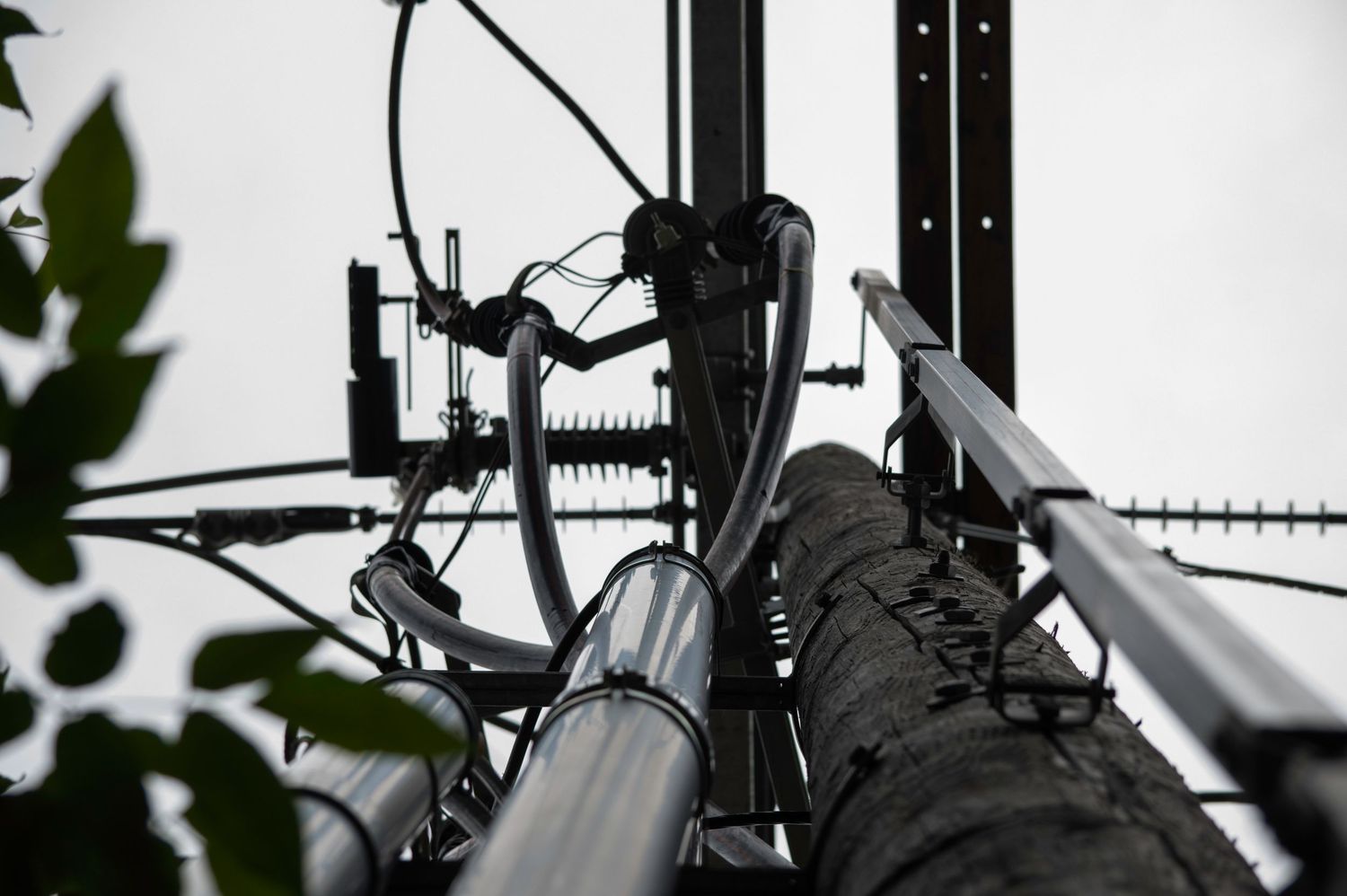 Close-up view of a telecommunications tower with cables, antennas, and metal components against a cloudy sky.