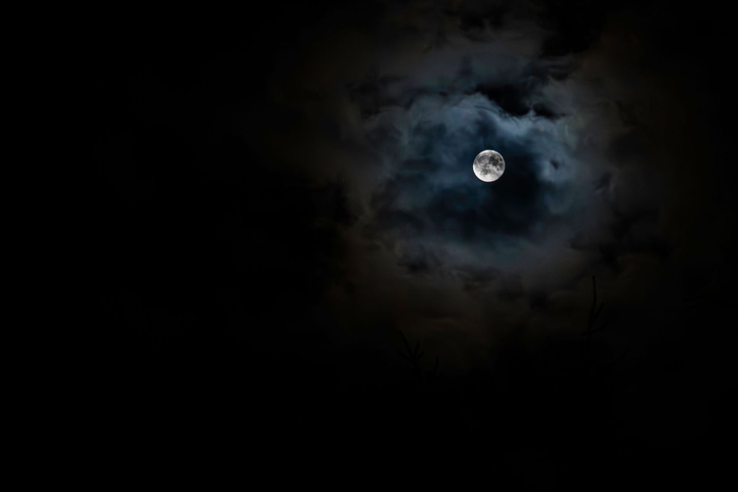 A full moon glowing through dark dramatic clouds in a night sky.