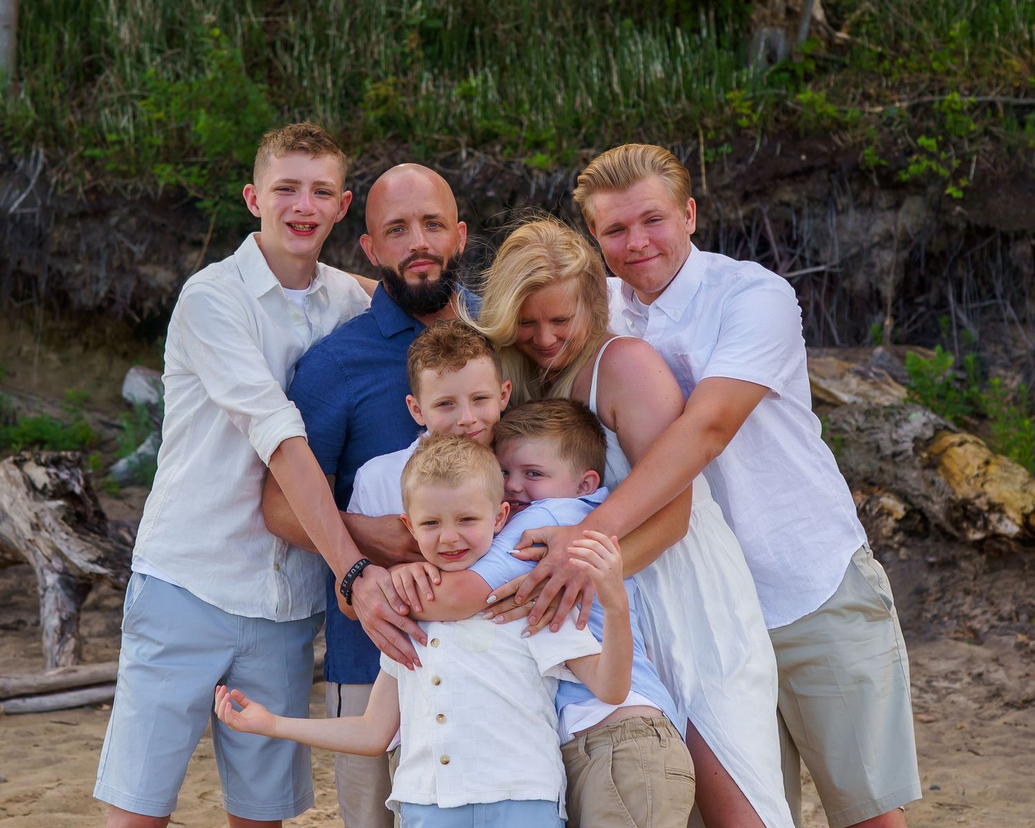 Happy family of six posing together on a sandy beach, wearing coordinated white and blue outfits.