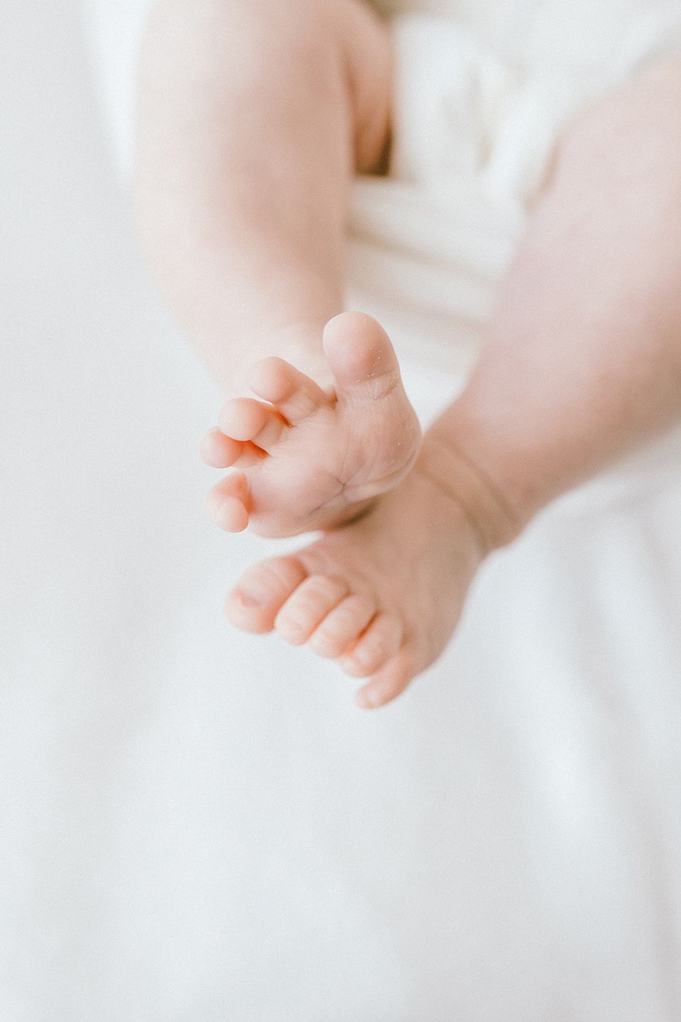 Close-up of tiny newborn baby feet and toes against a soft white background.