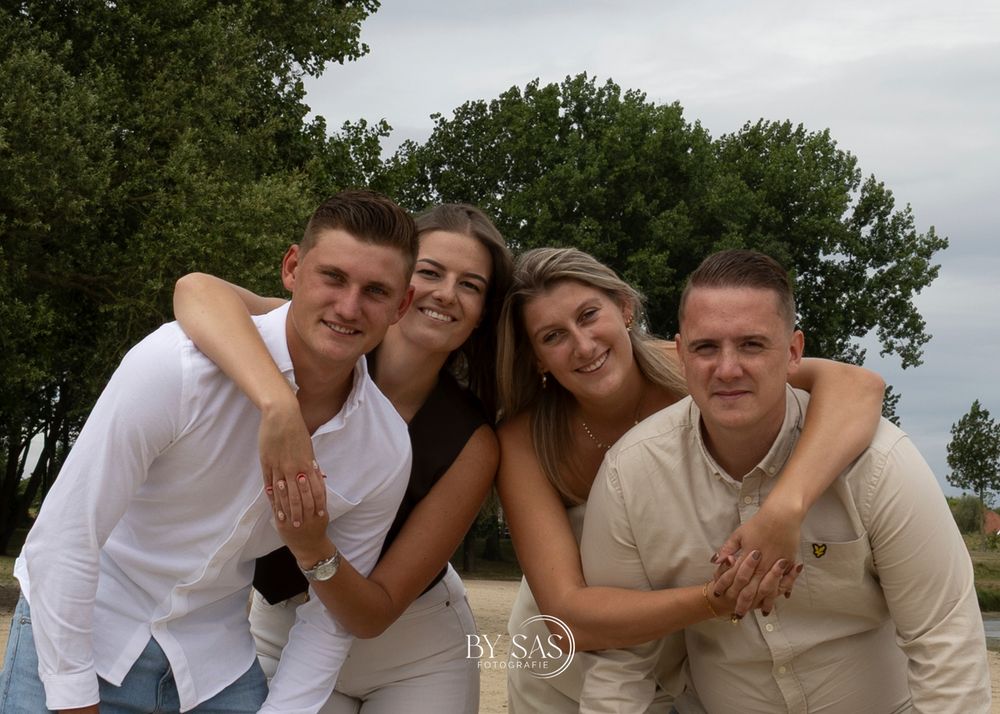 Four smiling young adults pose together outdoors near trees for a professional group portrait photo.