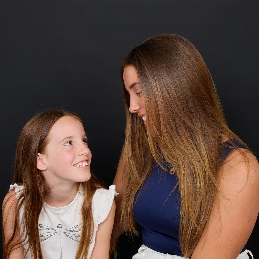 A young girl and teenage girl share a sweet moment looking at each other in a studio portrait.