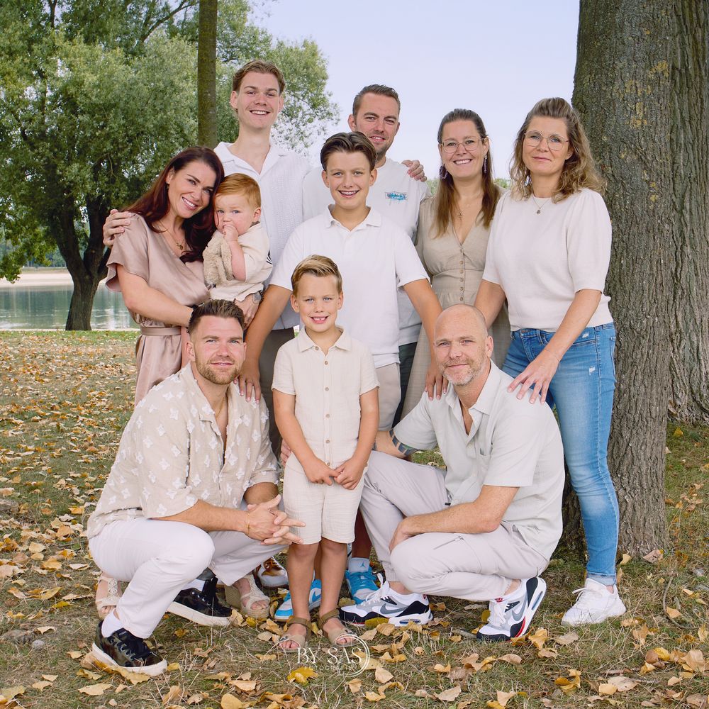 A large family group posing outdoors under a tree in coordinated neutral outfits during autumn.