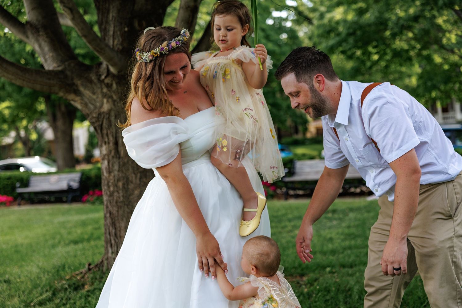 Joyful newlyweds celebrate outdoors in wooded wedding venue, bride in white dress and groom in blue shirt raising hands.