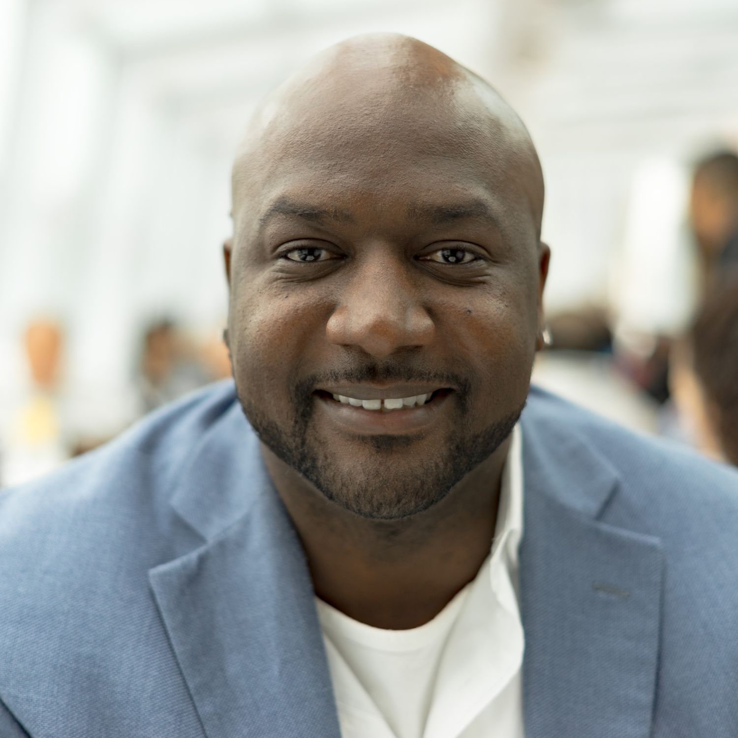 Smiling bald man in light blue blazer and white shirt at an indoor event.
