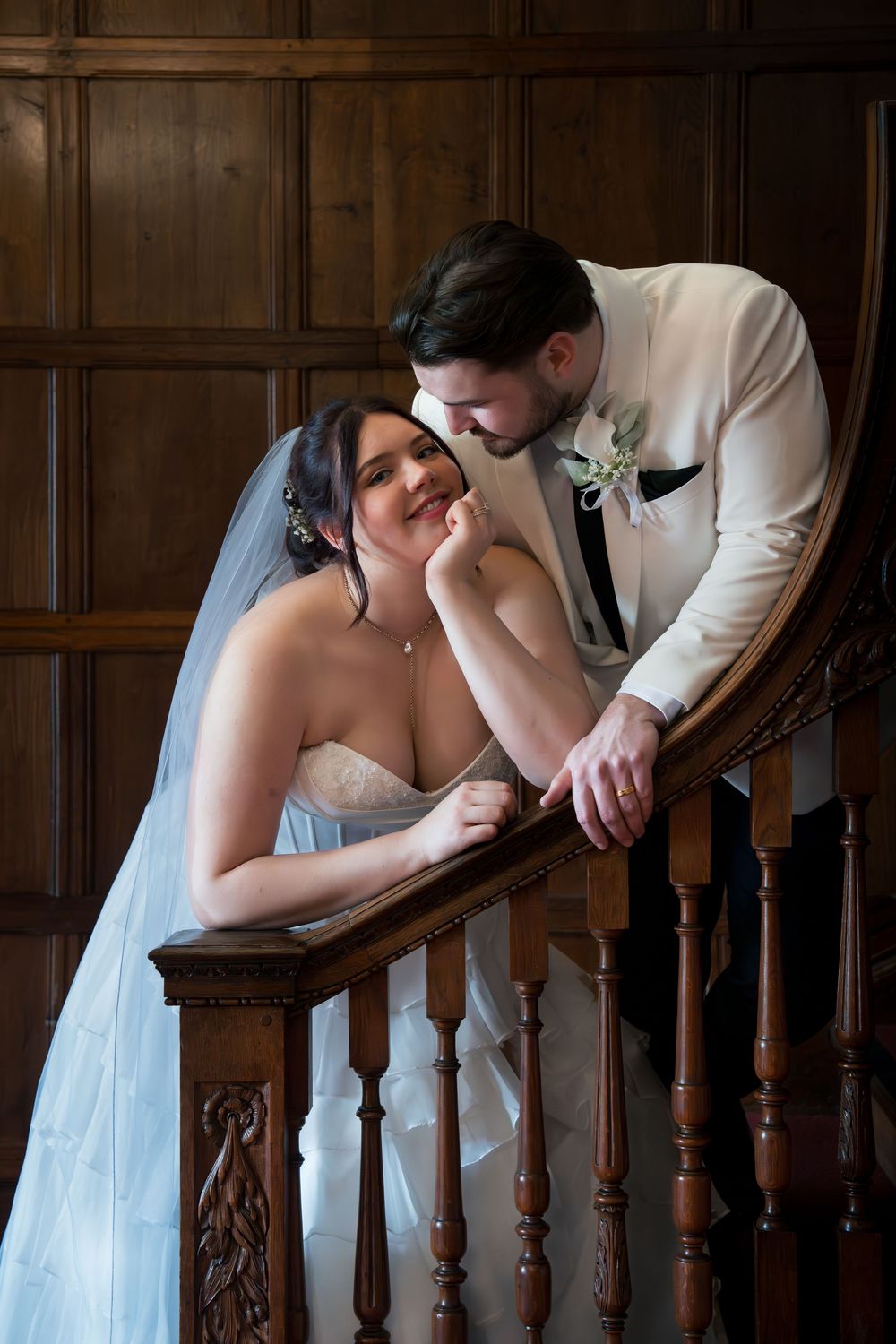 Bride and groom share a romantic moment on a wooden staircase, bride in blue gown with veil, groom in white suit.