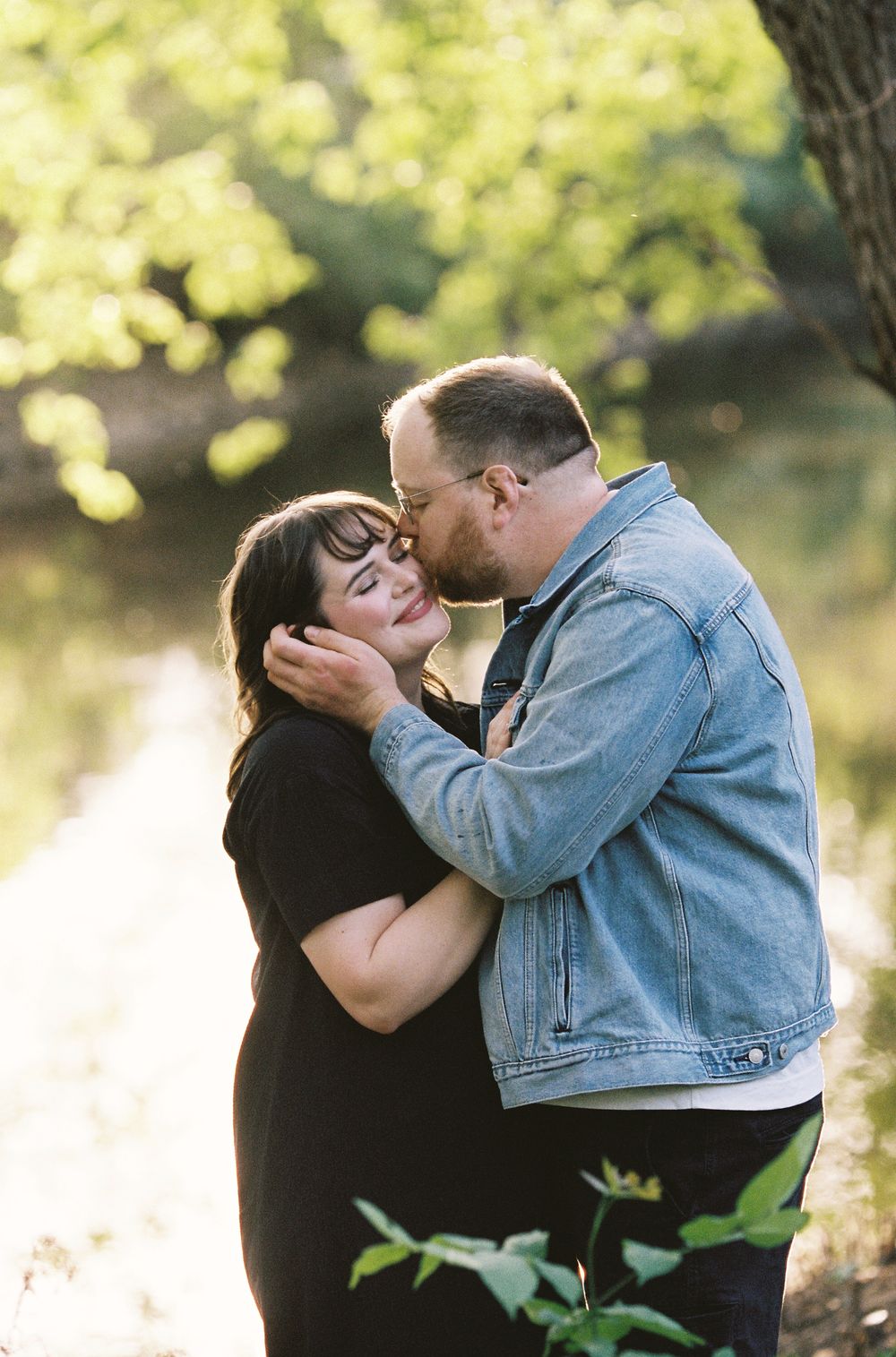 A man tenderly kisses a womans forehead as they embrace outdoors in soft natural light.