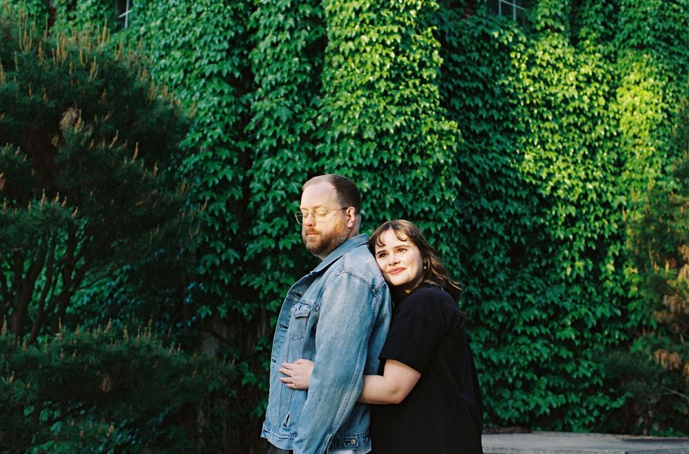 Couple embracing in front of lush green ivy covered wall in romantic outdoor portrait.