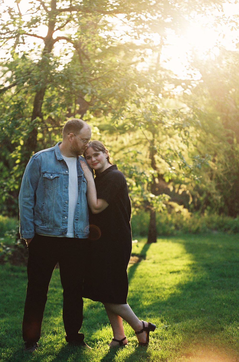 Couple sharing a romantic moment in a golden sunlit garden with lush green trees.