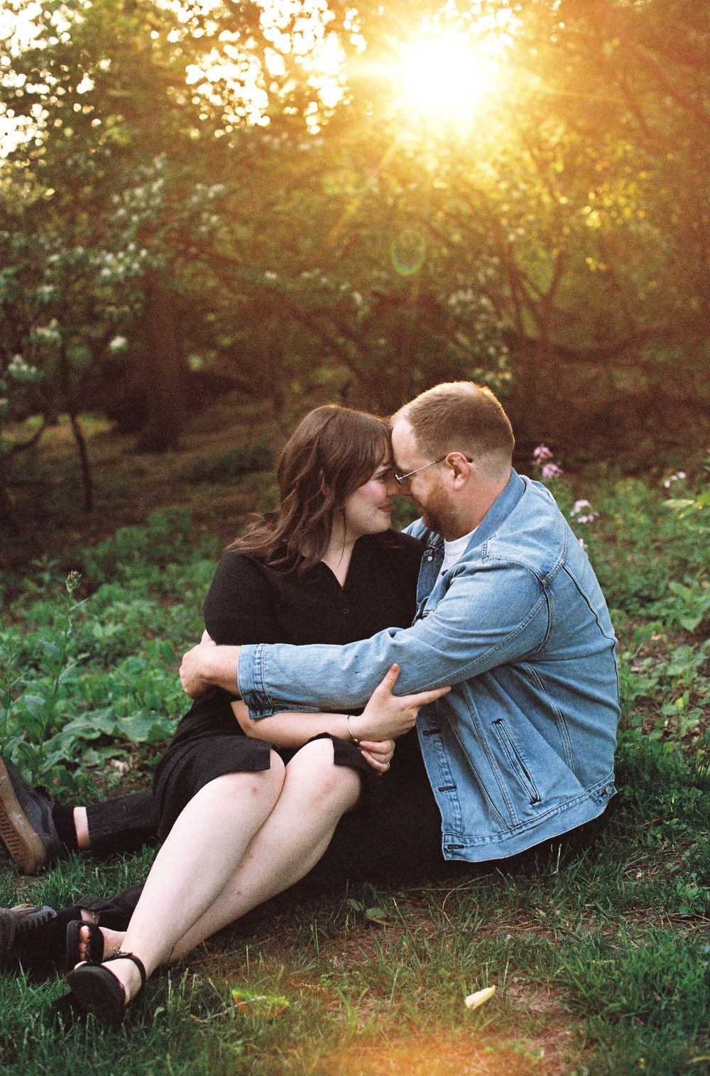 Couple sitting close together on grass sharing a tender moment in warm sunset light.