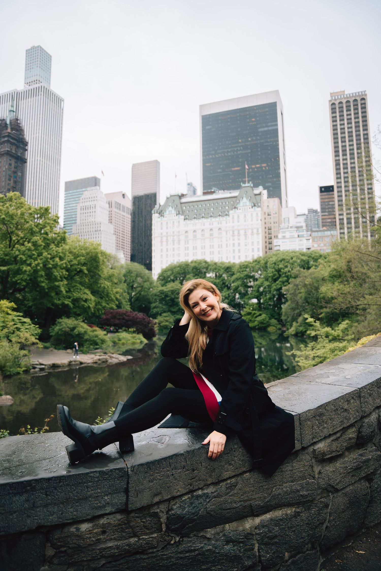 Relaxed pose on stone wall in Central Park with Manhattan skyline backdrop.