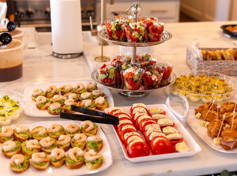 Elegant party appetizer spread featuring caprese skewers, stuffed strawberries, and assorted finger foods on a white marble counter.
