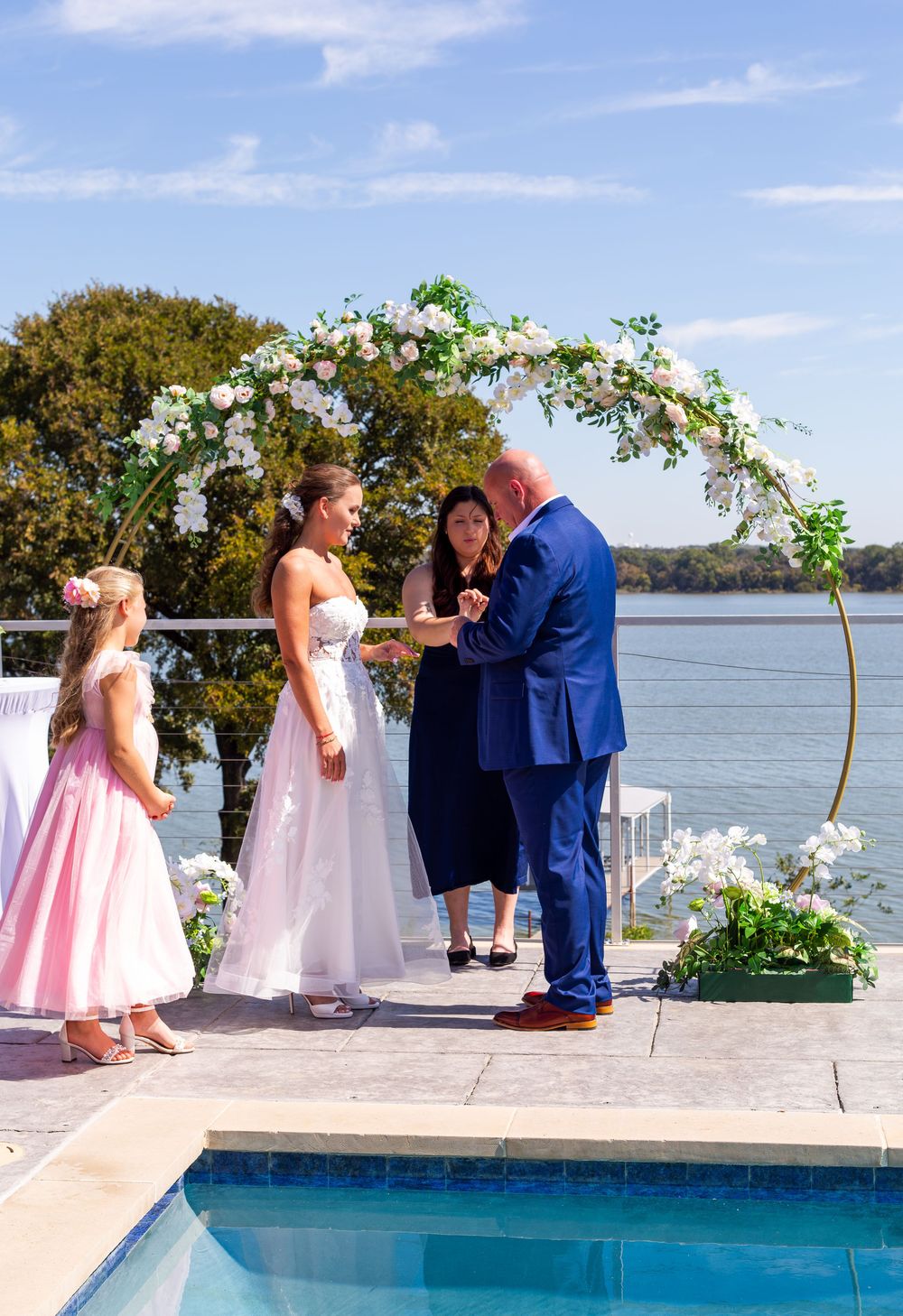 Bride and groom exchanging vows at outdoor waterfront wedding ceremony with floral arch.