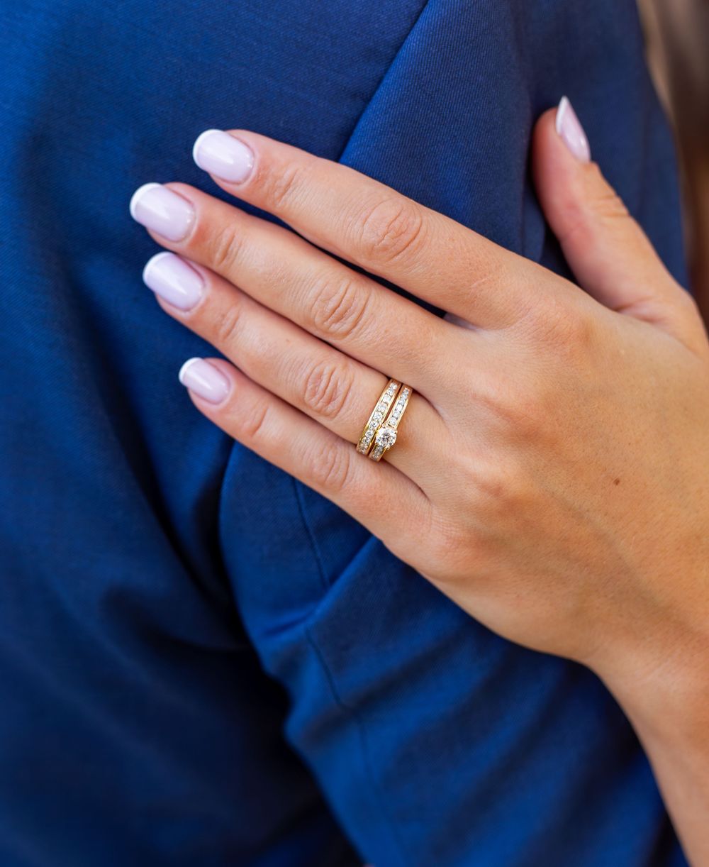 Close-up of a womans hand with gold diamond wedding rings resting on a blue suit.