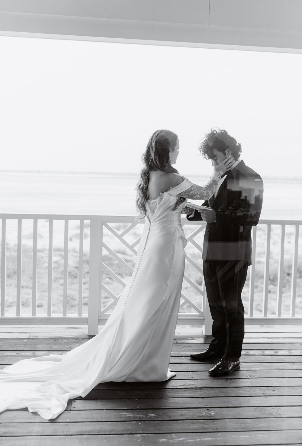 Bride and groom share intimate vow exchange on oceanfront deck in black and white photo.