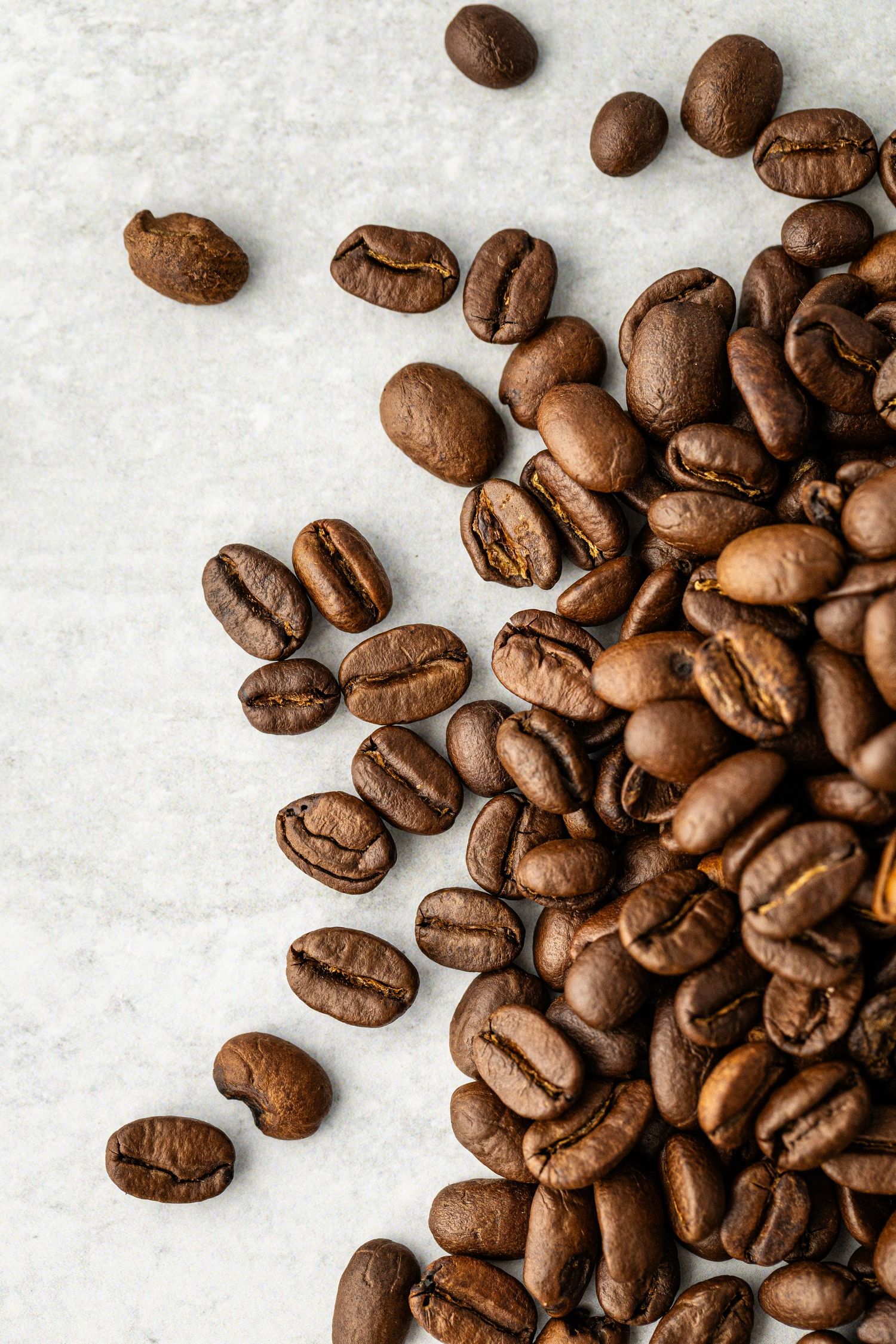 Close up photo of spilled coffee beans against a clean marble background by Bella Priscilla Photography.