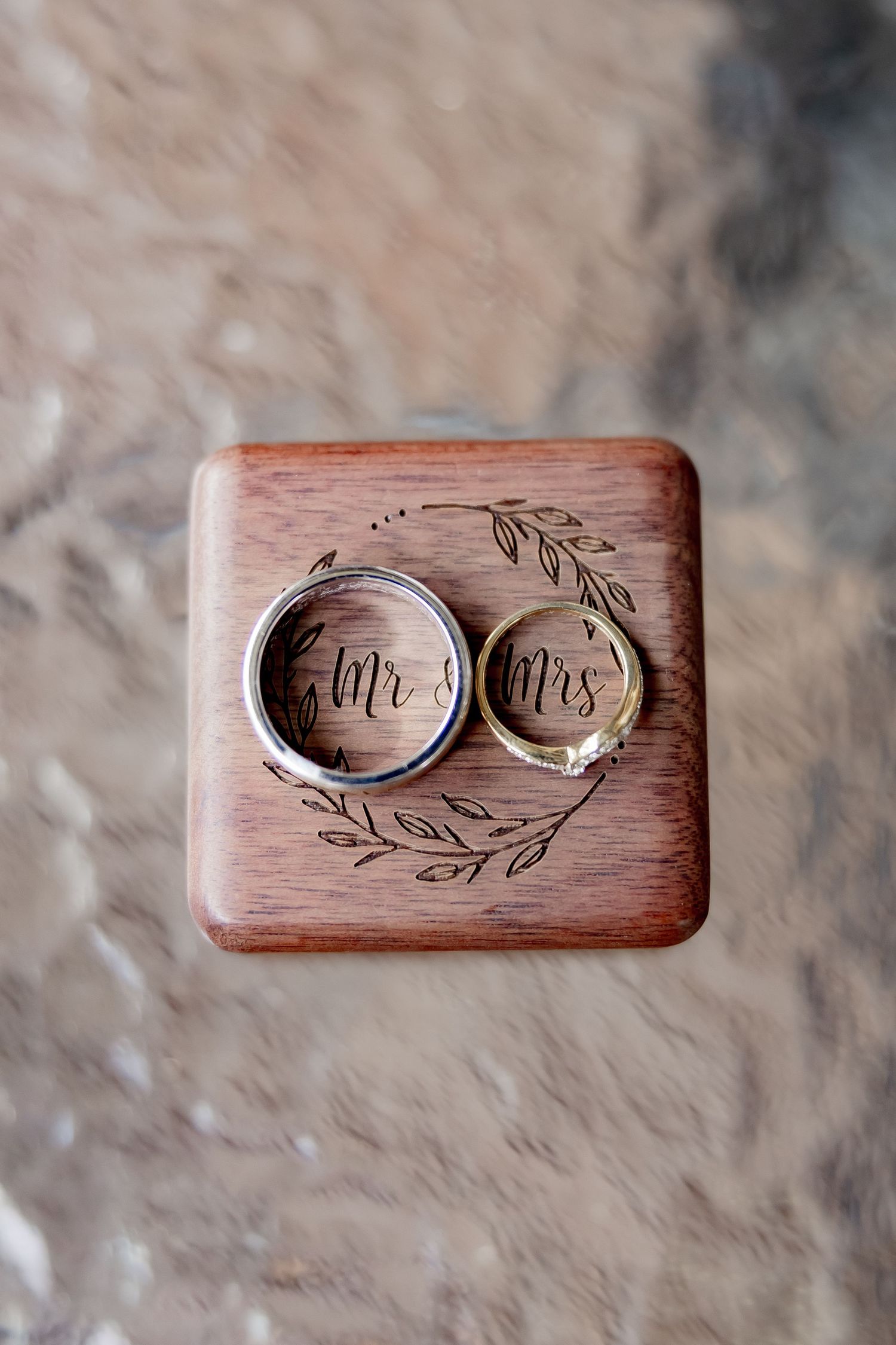 Wedding rings for Mr and Mrs displayed in an engraved wooden ring box with floral detailing.