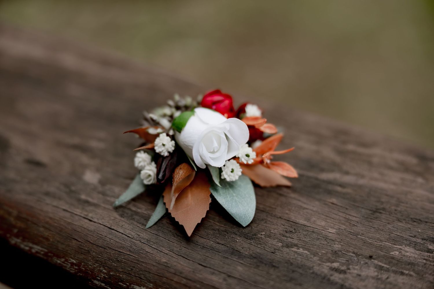 Wedding boutonniere with white rose, red berries, and autumn leaves on rustic wood.