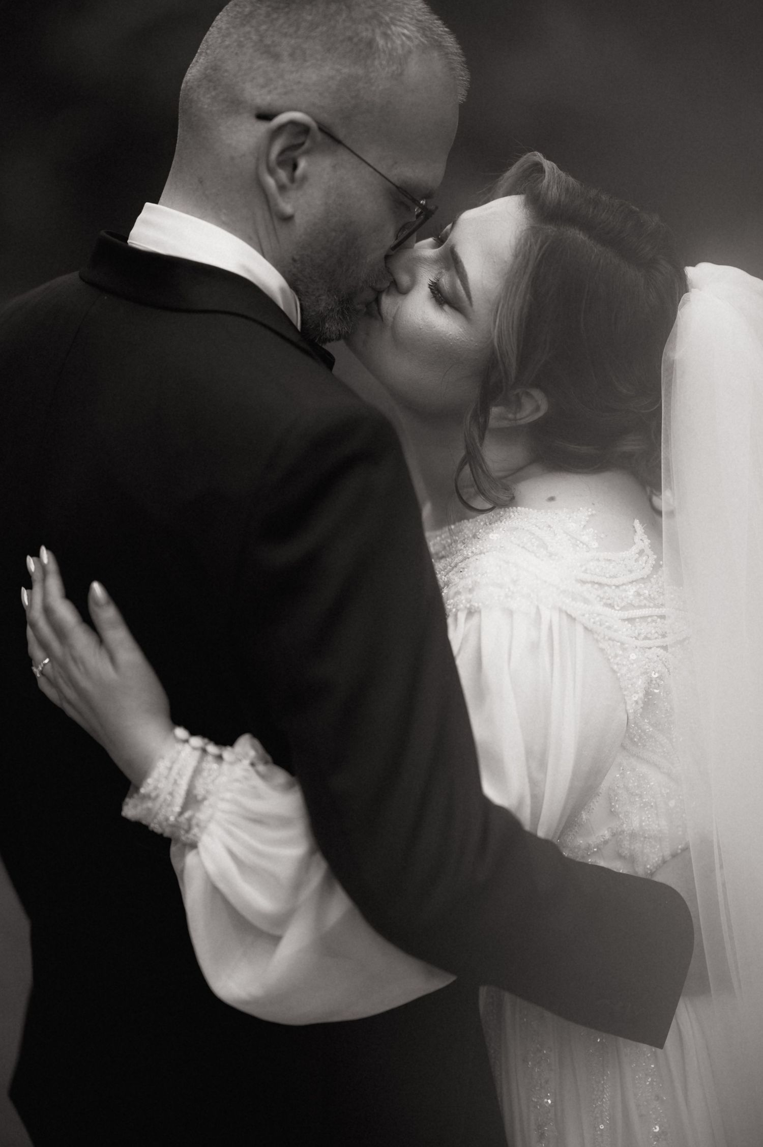 Black and white wedding photo of bride and groom sharing a romantic kiss, bride in white gown with veil.