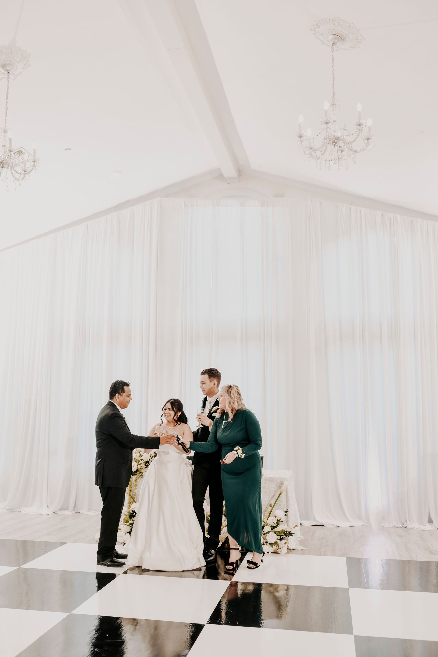 a bride and groom listen to speeches by their parents at their wedding