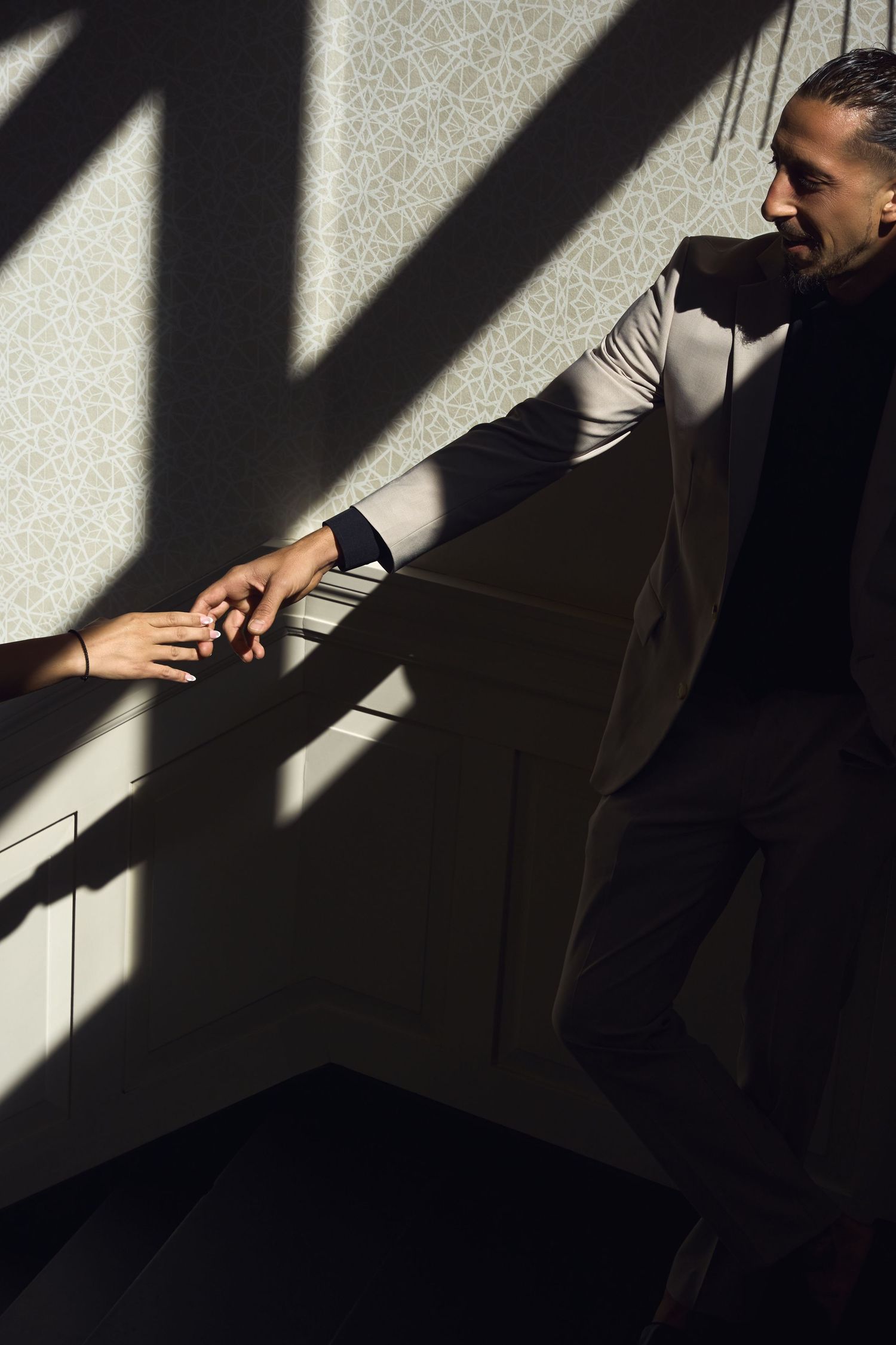 Man in dark suit reaching out to touch a woman's hand in dramatic light and shadow.