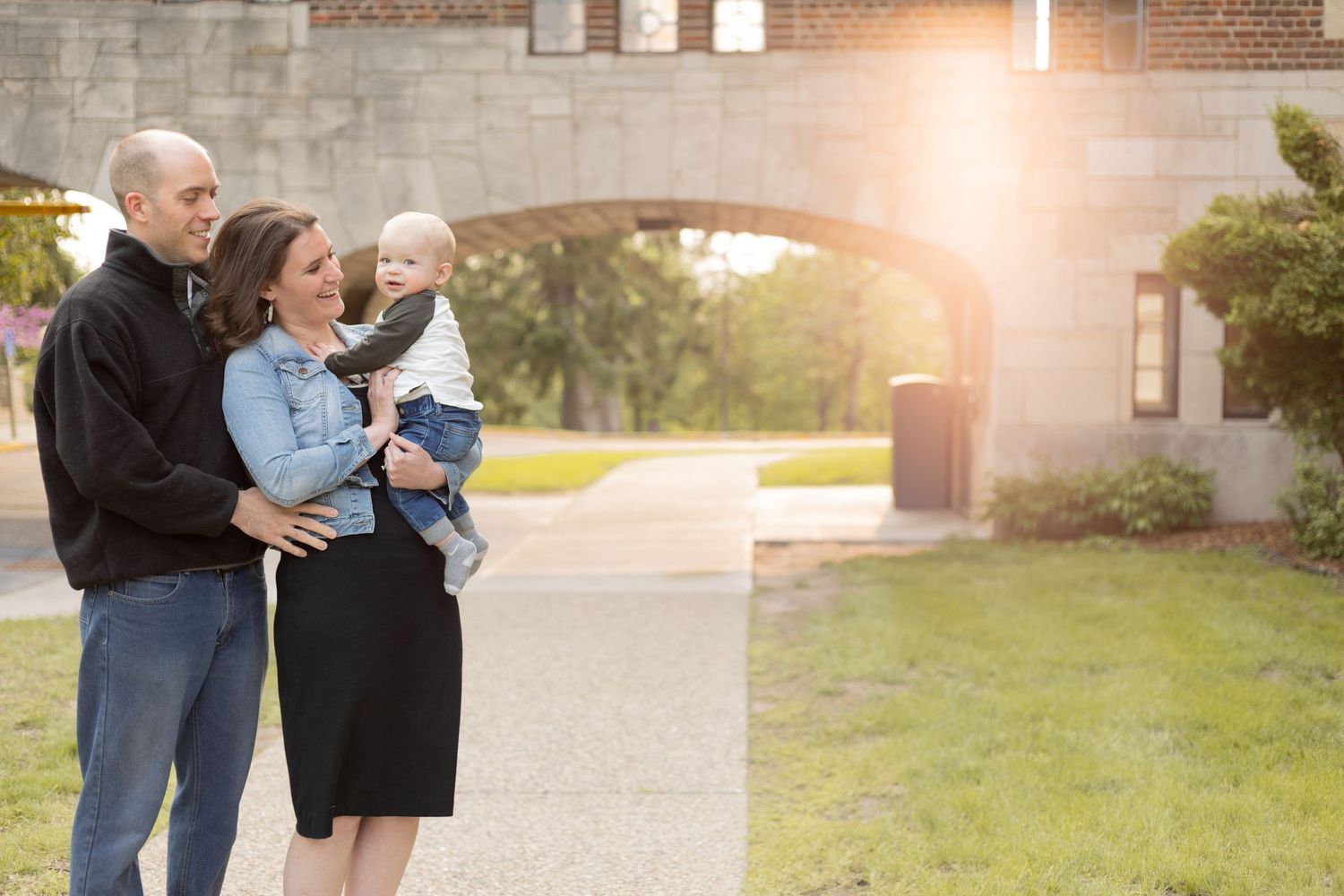 Family of three standing together under architectural bridge in park setting.