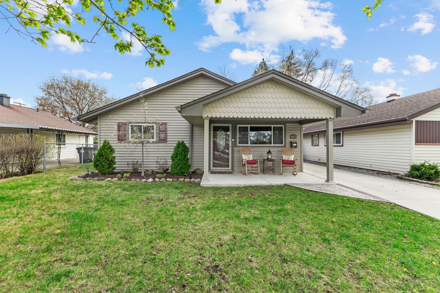 Charming single-story gray home with covered front porch, lush green lawn, and mature trees in spring.