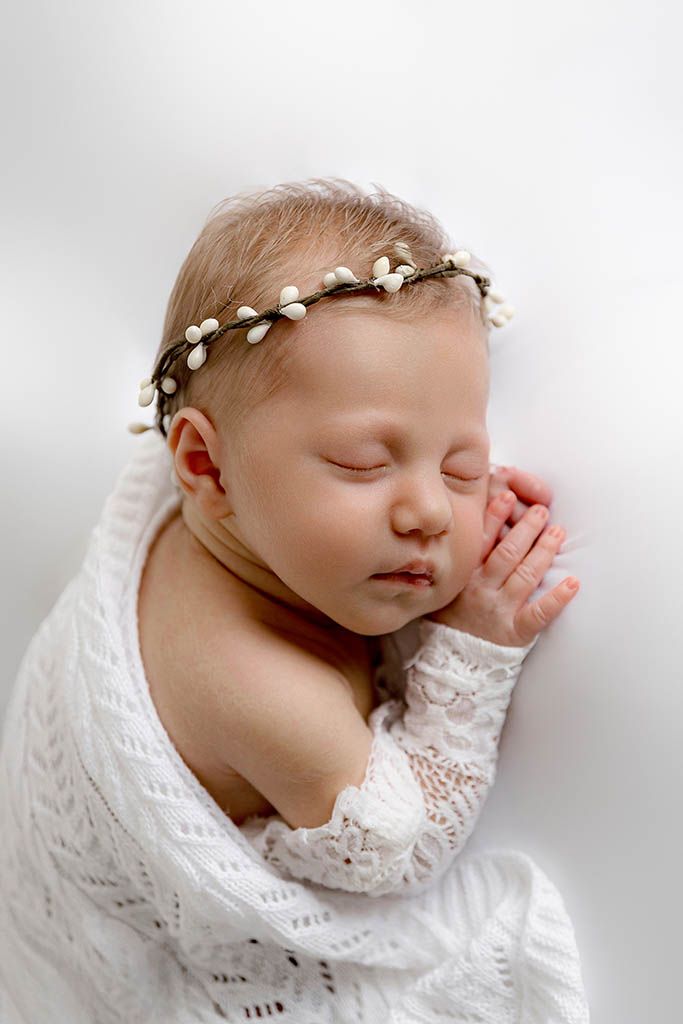 Close-up of sleeping newborn baby girl wrapped in white knit blanket wearing delicate pearl flower crown.
