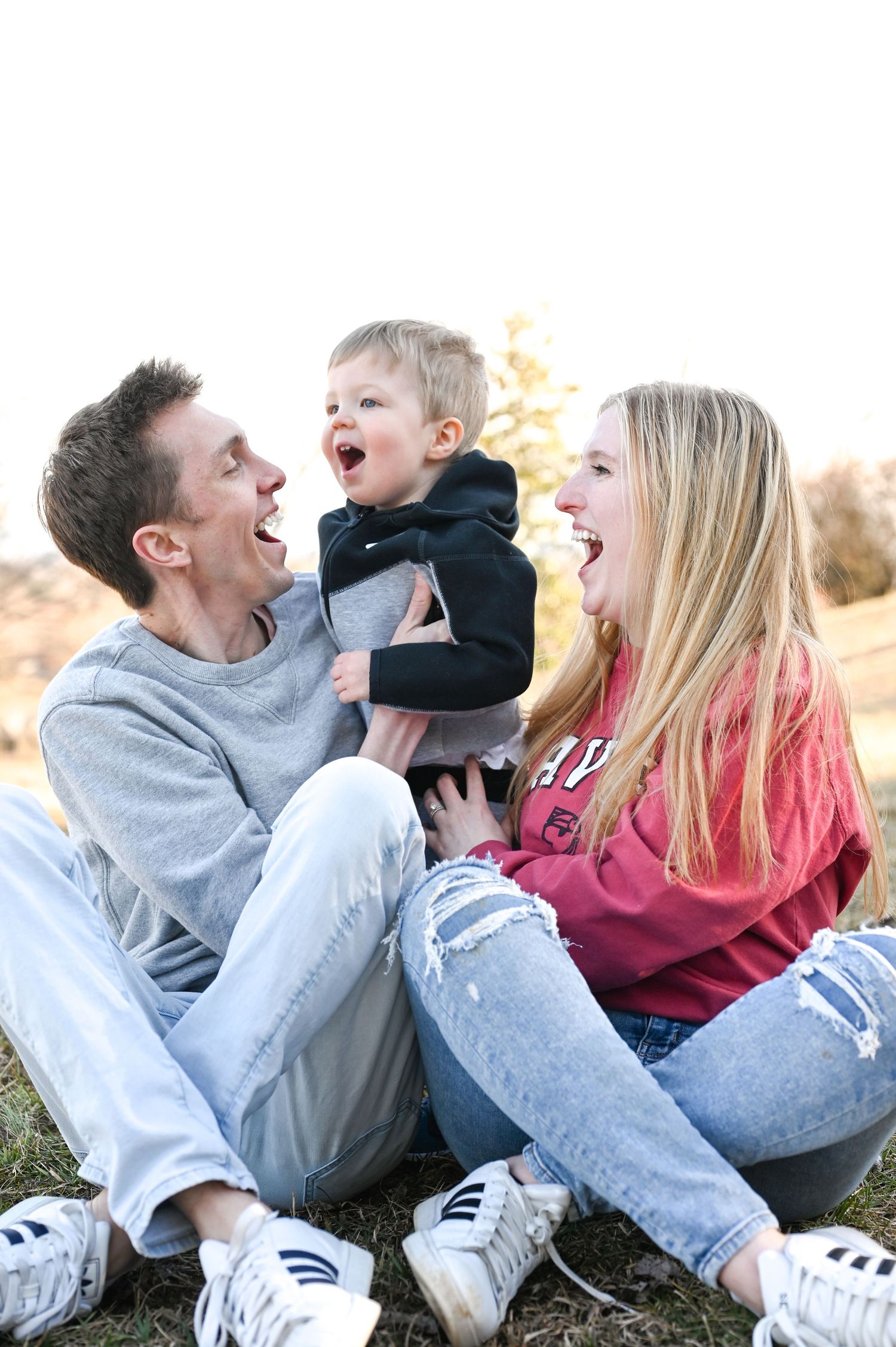 Family laughing together on grass during playful outdoor photo session.