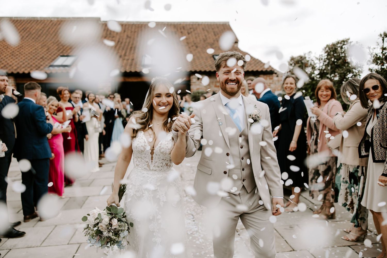 A joyful wedding celebration with guests tossing confetti as the newlyweds walk through an outdoor venue.