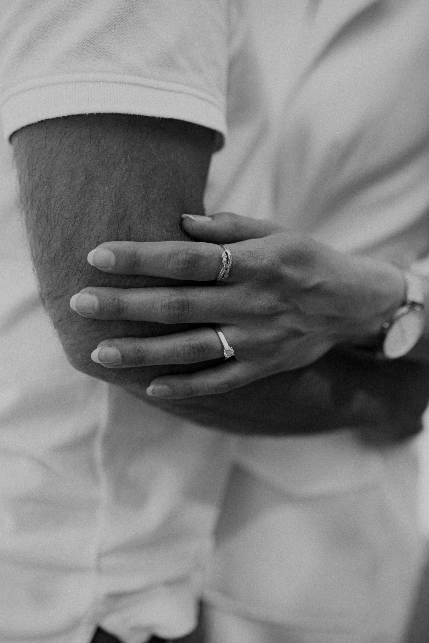 Black and white close-up of a woman's hand with engagement ring resting on a man's arm.