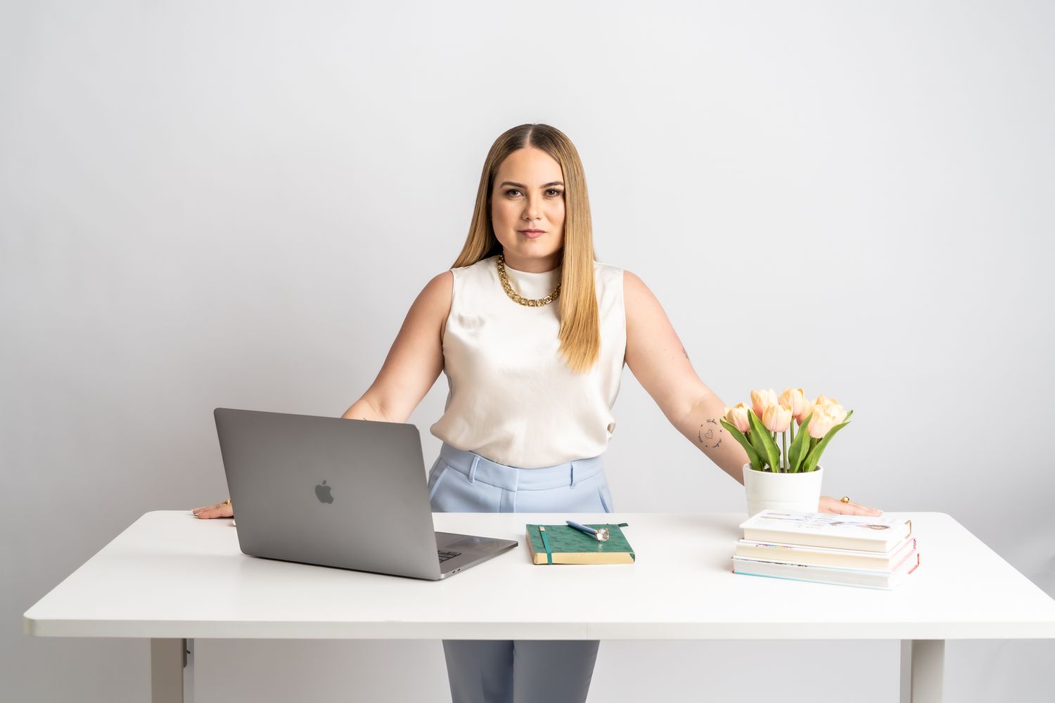 Professional woman works at clean white desk with laptop and tulips in modern office setting.