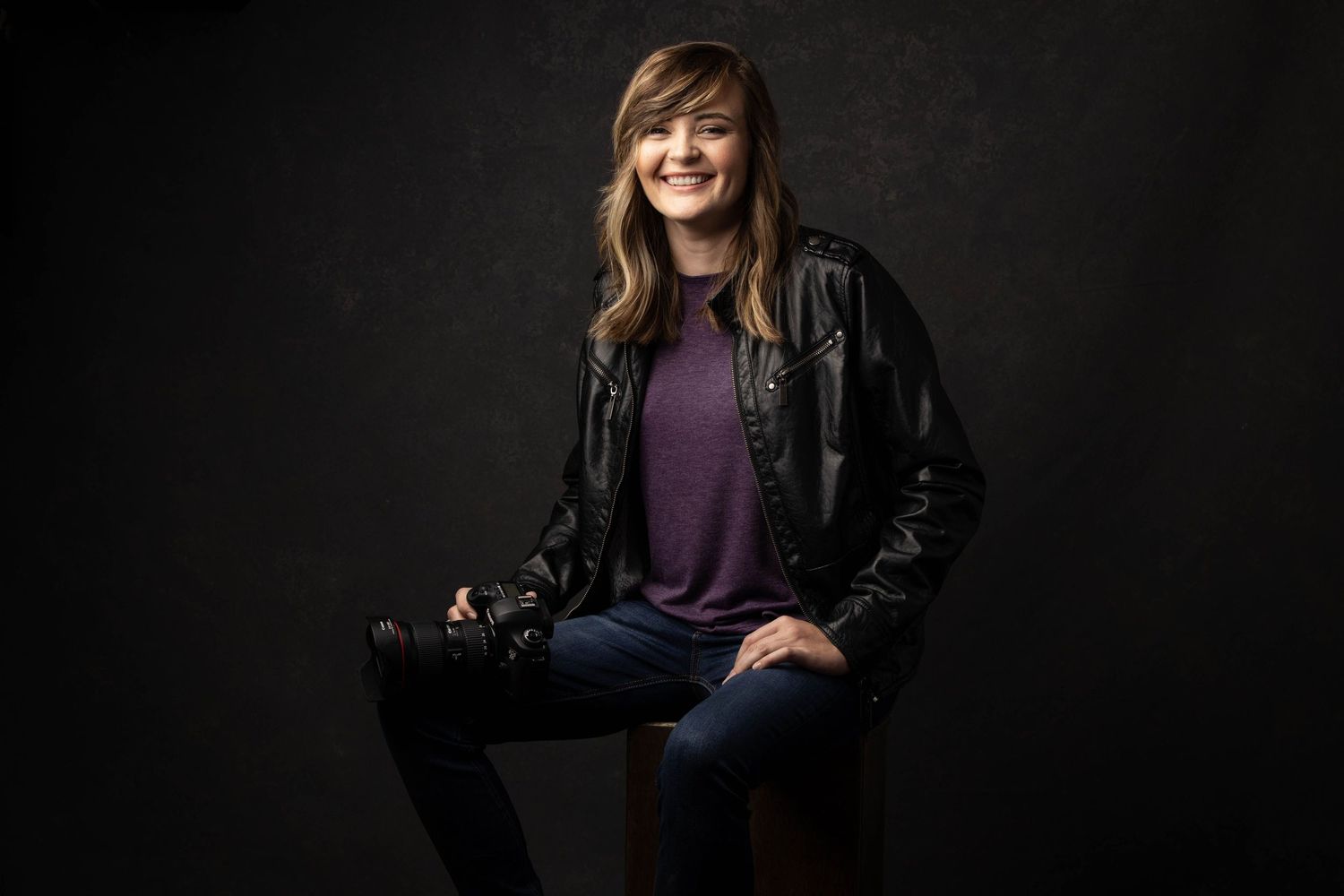 Studio portrait of photographer Heather Carpenter against dark background featuring leather jacket and casual attire.