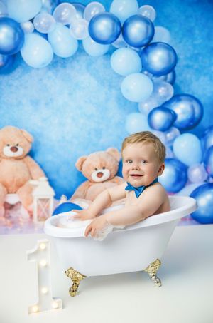 Baby bath photo setup with decorative blue balloon arch, number one light, and teddy bears against blue background.