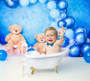 A bathtub scene with teddy bears and blue balloons arranged against a bright blue backdrop for a baby photoshoot.