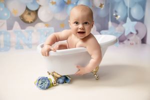 Sweet baby poses on white backdrop with blue ornaments and dreamy clouds in a holiday studio setting.