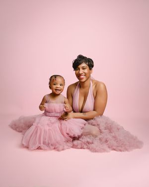 Parent and child wearing matching pink tulle dresses pose together against pink background for portrait session.