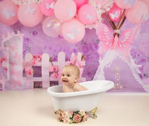 Pink and purple fantasy themed bath setup with vintage tub, balloons, butterflies and flower decorations.