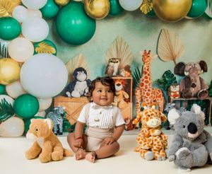 Festive party setup with green and gold balloon garland, plush animals, and stuffed toys arranged against a teal backdrop.