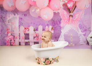 Pink and purple balloon-decorated backdrop with a bathtub scene featuring floral decor and whimsical butterfly details.
