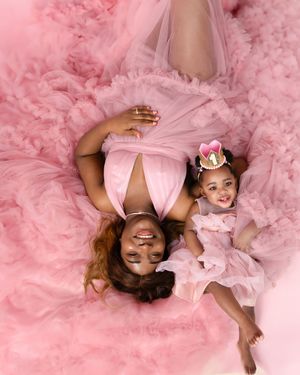 Mother and daughter wearing matching pink tulle dresses lay on fluffy pink backdrop during portrait session.