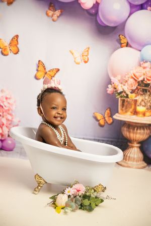 A whimsical bath photography setup with purple balloons, orange butterflies, and pink floral decorations.