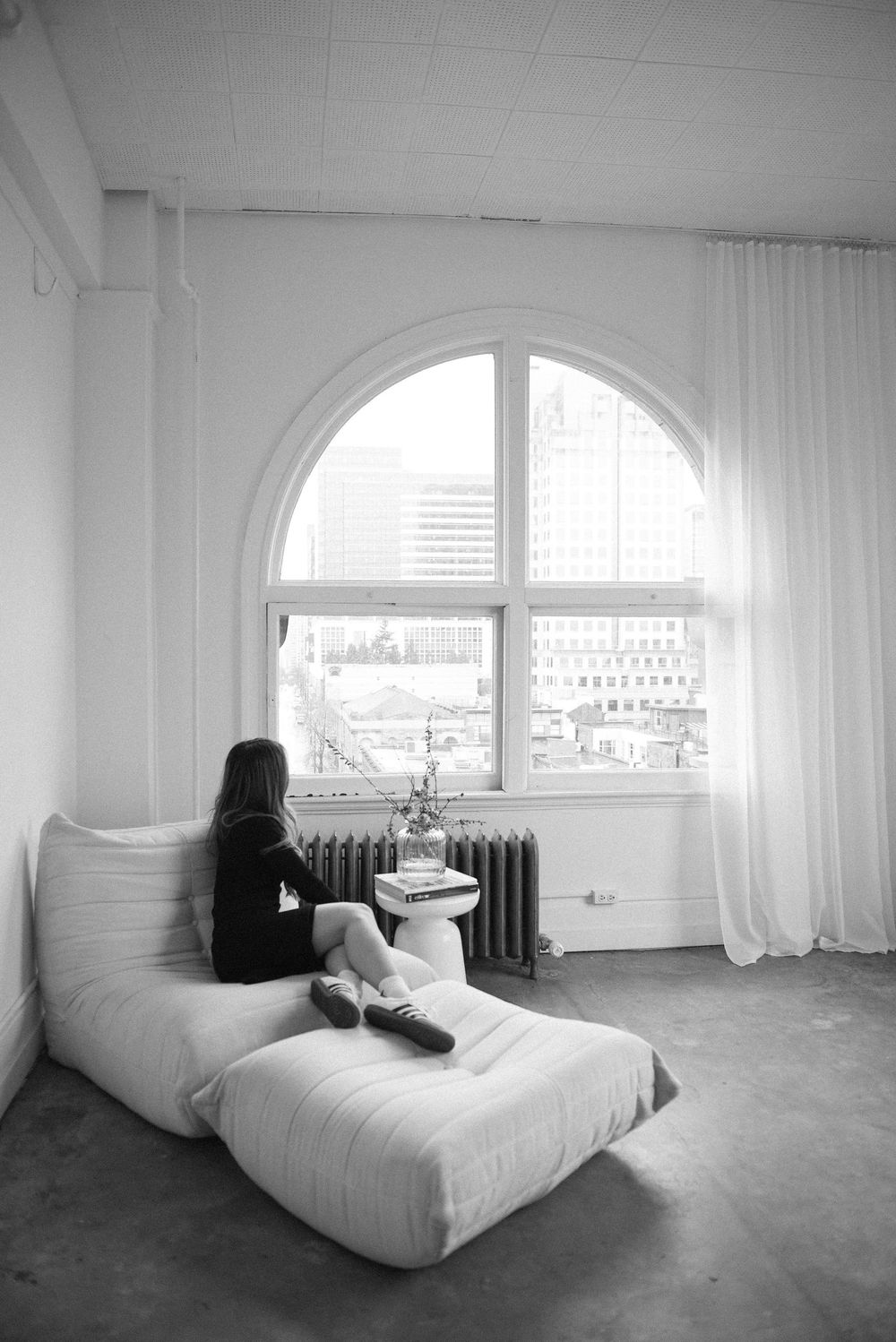 Minimalist room interior with person relaxing on white furniture near arched windows.