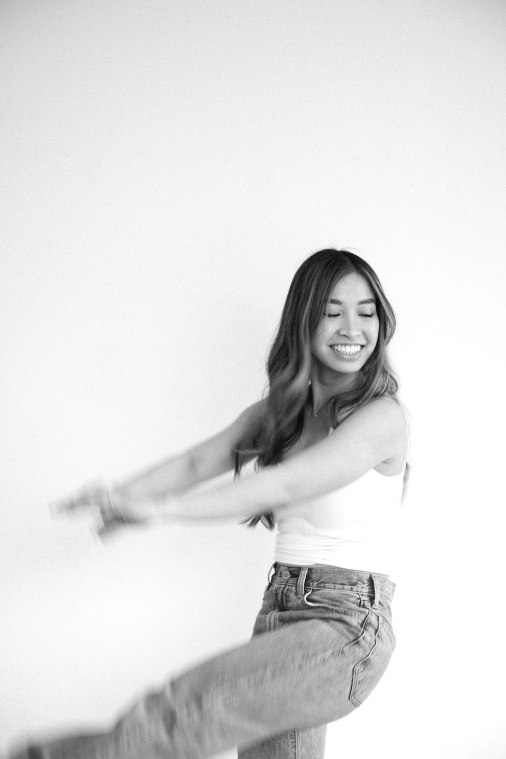 Dynamic motion blur captures dance movements in white top and jeans against minimalist backdrop.