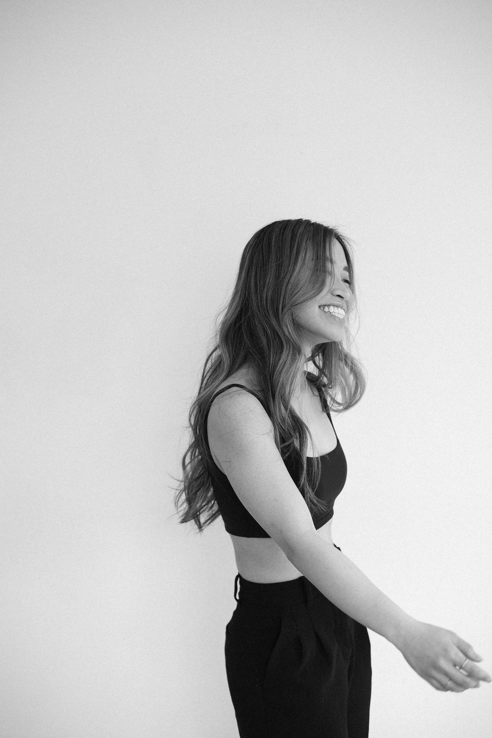 Black and white artistic portrait of someone in dark clothing dancing joyfully against a white backdrop.