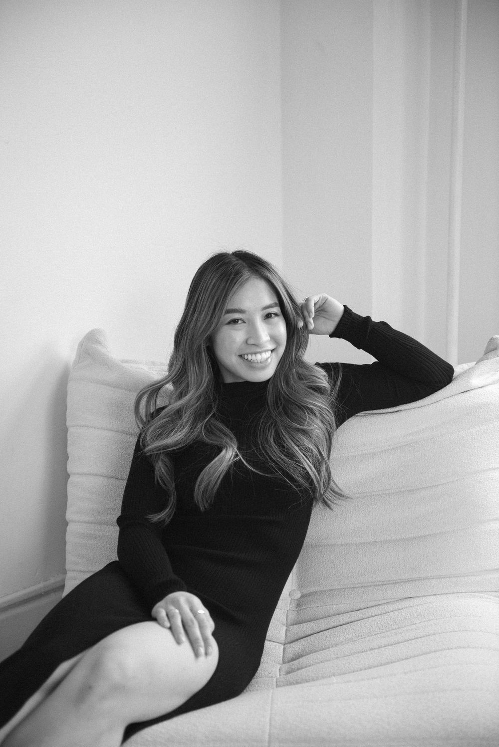 Person in black dress lounging casually on white furniture in artistic photoshoot.