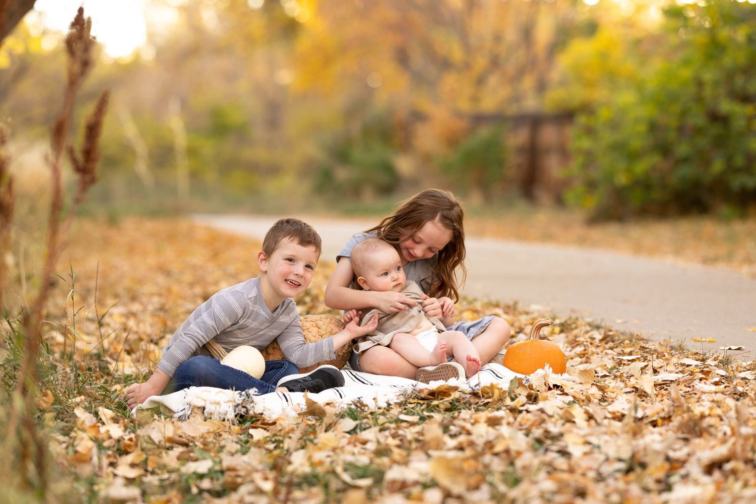 Children playing together in fallen autumn leaves at sunset with orange pumpkins on a nature path.