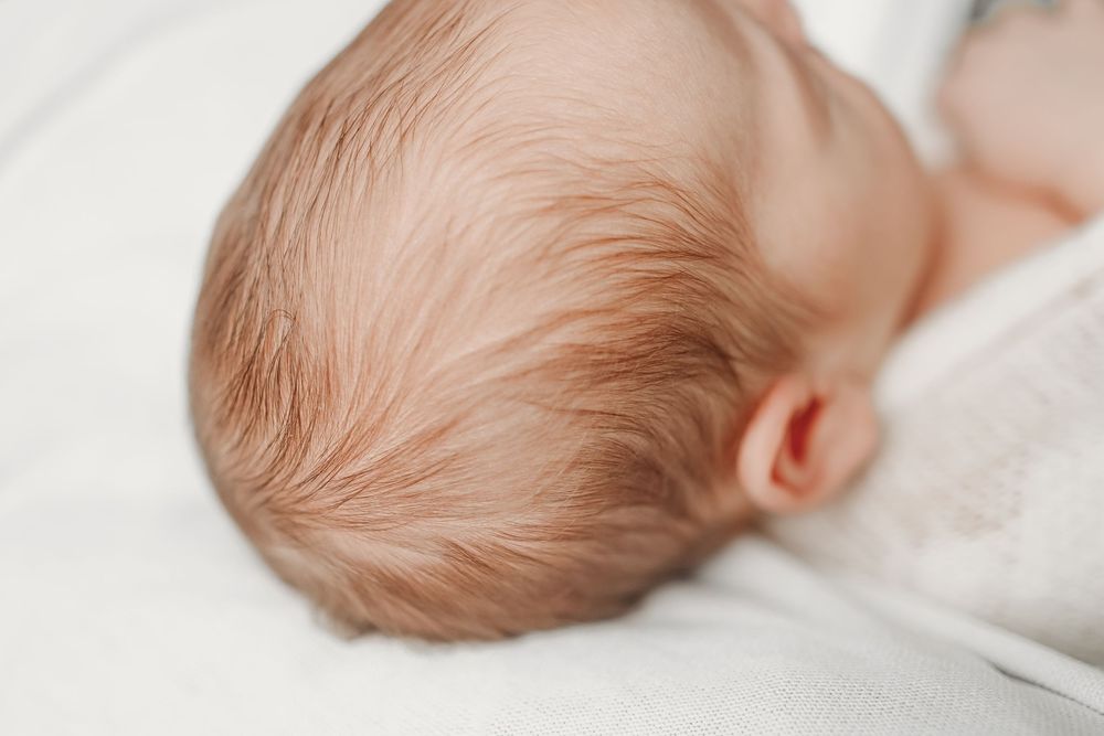 Sleeping infant with light hair rests peacefully against soft white bedding.