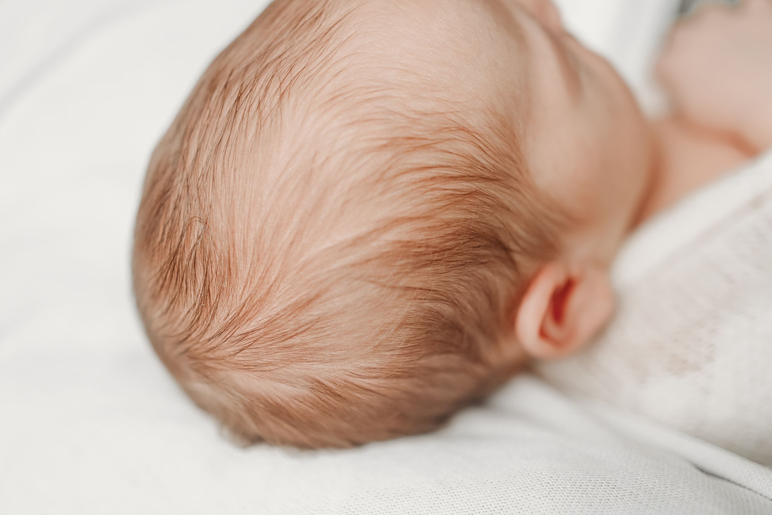 Sleeping infant with light hair rests peacefully against soft white bedding.